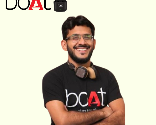 Portrait of Aman Gupta, co-founder of boAt, wearing a boAt company t-shirt. The background is cream-colored with the boAt company logo displayed on the top left side.